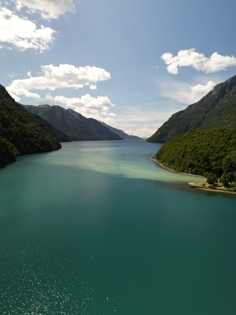 Brazo del lago de aguas turquesas entre montañas de bosque, visto desde el dron