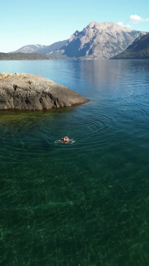 Nadando en aguas transparentes junto a una roca, con la cordillera de fondo