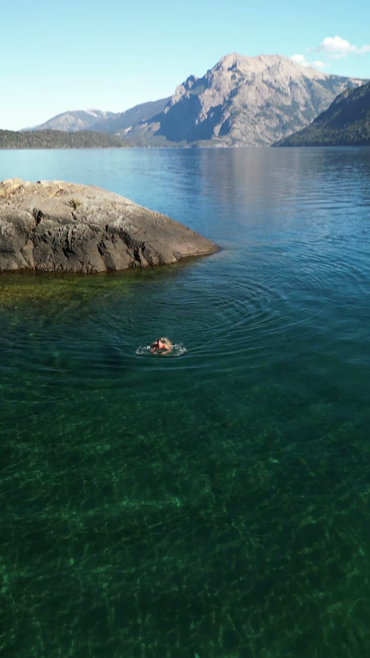 Nadando en aguas transparentes junto a una roca, con la cordillera de fondo