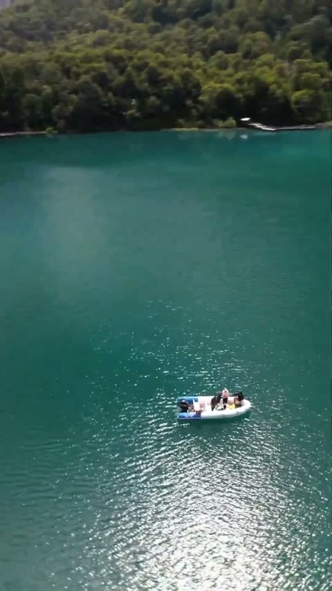 Vista con dron de la lancha sobre agua turquesa, subiendo hacia los cerros