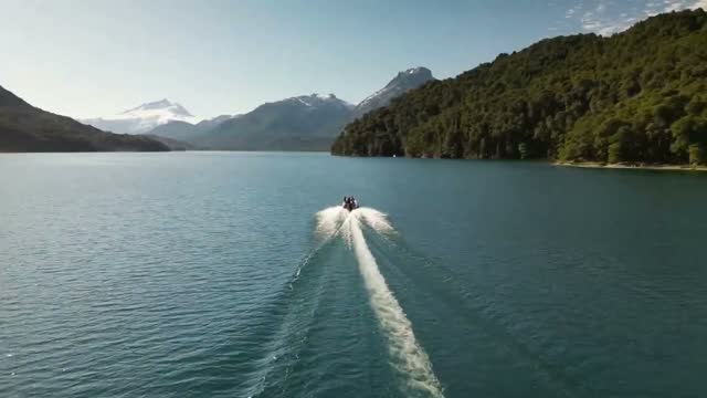 La lancha abriendo estela en el lago, con bosque y cerros nevados de fondo